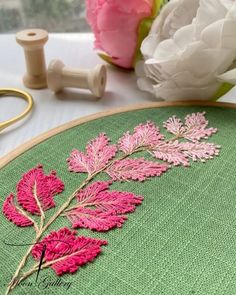 a close up of a embroidery on a table with flowers in the background and a sewing needle