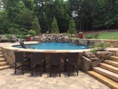 a pool surrounded by stone steps and patio furniture in the middle of an outdoor area