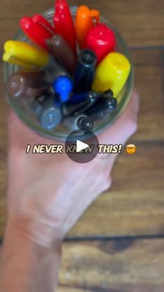 a hand holding a glass container filled with colorful plastic toys on top of a wooden table