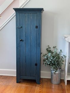 a tall blue cabinet next to a plant in a room with wooden floors and stairs