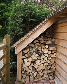 a pile of logs sitting in the corner of a building next to a fence and trees