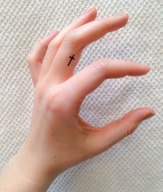 a person's hand with a small cross tattoo on it