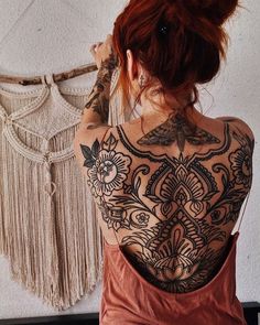 a woman with tattoos on her back standing next to a wall