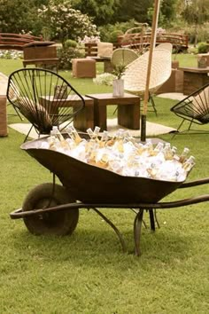 an old wheelbarrow filled with bottles and empty wine glasses sitting on the grass