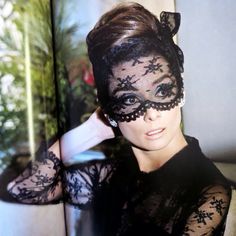 a woman wearing a black lace mask and posing for a photo in front of a window