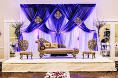 the stage is decorated with purple drapes and gold furniture for an elegant wedding reception