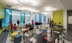 children are sitting at desks in an open area with large windows and bright green walls