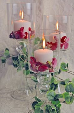 three candles are sitting in glass vases with flowers and leaves on the table next to each other