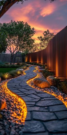 a stone path leading to a fence with trees and bushes in the background at sunset