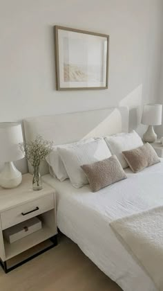 a bed with white sheets and pillows in a bedroom next to a painting on the wall