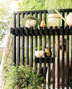 a woman standing next to a black fence with potted plants on top of it