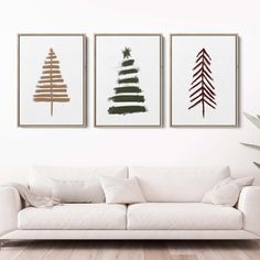 three framed christmas trees are hanging on the wall in a living room with white furniture