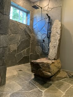 a stone shower in a bathroom with a rock on the floor and a window above it