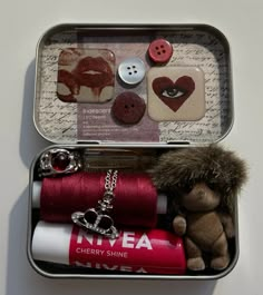 an open tin with buttons, thread and a teddy bear in it's lap