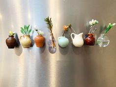 five vases are lined up on the side of a refrigerator with flowers in them