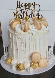 a birthday cake with white frosting and macaroons on the top is decorated with gold foil