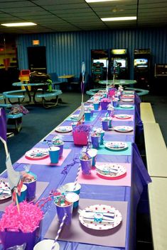 a long table set up with purple and blue plates, cupcakes and candy