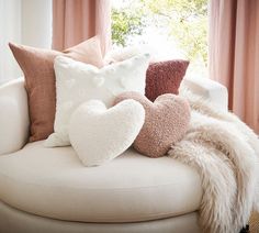 pillows are arranged on the back of a white chair in front of a window with pink drapes