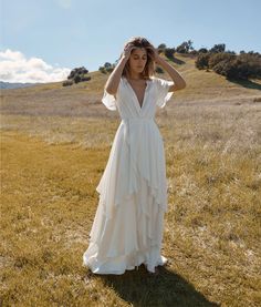 a woman in a white dress is standing on the grass with her hands behind her head