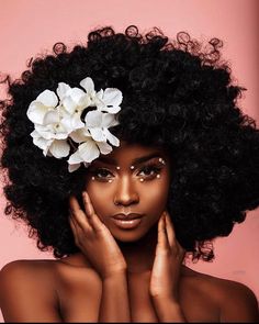 a woman with an afro and flowers in her hair is posing for the camera on a pink background