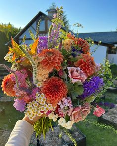 a person holding a bouquet of flowers in front of a house with grass and trees