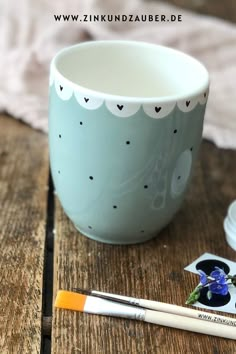 a cup sitting on top of a wooden table next to two markers and a pen