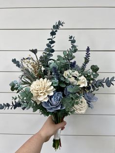 a person holding a bouquet of flowers in front of a white wall with green leaves