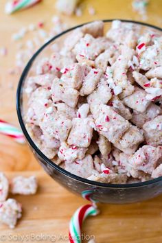 a glass bowl filled with candy canes and white chocolate puppy chow next to some candy canes