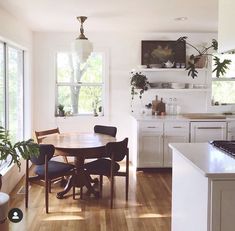 a dining table and chairs in a room with wood flooring, white cabinets and windows