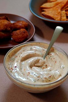 a bowl filled with dip next to plates of chips and dipping sauce on a table