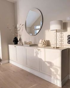 a white dresser sitting next to a large mirror on top of a wooden floor in a living room