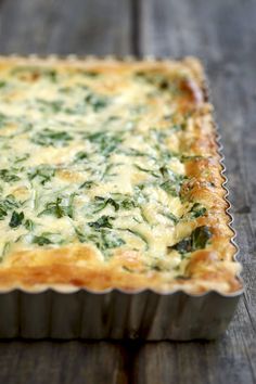 a quiche with spinach and cheese in a metal pan on a wooden table