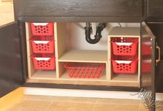 some red baskets under a wooden shelf on the floor next to a black drain faucet