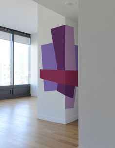 an empty room with purple and pink squares on the wall, next to a window