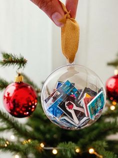 a hand is holding a christmas ornament in front of a tree with ornaments