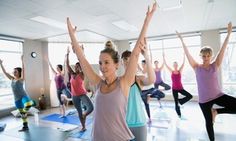 a group of people doing yoga in a large room with their arms up and hands raised