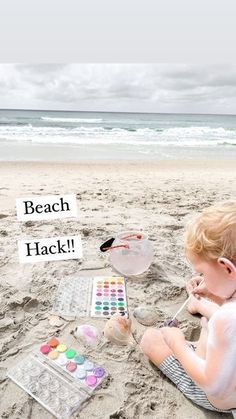 a young boy sitting on top of a sandy beach next to an ocean painting palette