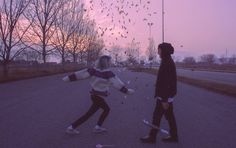 two people are walking down the street with their skateboards in hand and confetti falling from the sky