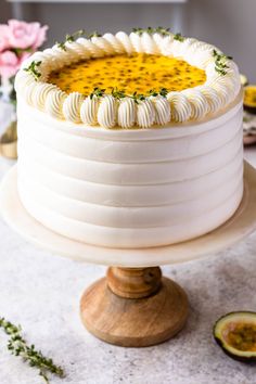 a white cake with yellow flowers on top sitting on a wooden stand next to sliced avocado