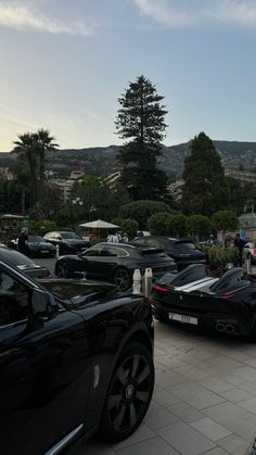 several cars parked in a lot with people walking around them and trees on the other side