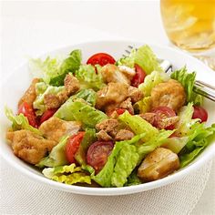 a white bowl filled with salad next to a fork and glass of beer on top of a table