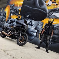 a man standing next to a motorcycle in front of a wall with graffiti on it