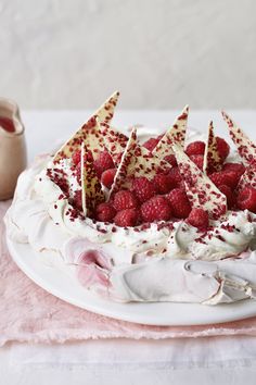 a white cake with raspberries and whipped cream on top is sitting on a pink tablecloth