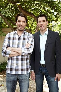 two men standing next to each other in front of a tree and fence with their arms crossed