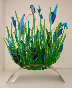 blue flowers and green grass in a clear glass vase on a white shelf against a white wall