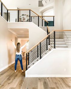 a woman standing in the middle of a living room next to a stair case and clock