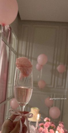 a person holding up a wine glass with pink balloons in the background