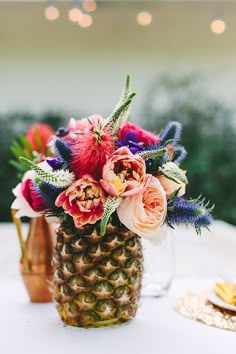 a pineapple vase filled with colorful flowers on top of a white table covered in lights