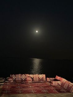 the moon is setting over the ocean with many pillows