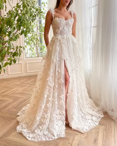 a woman in a white wedding dress with flowers on the skirt is standing near a window